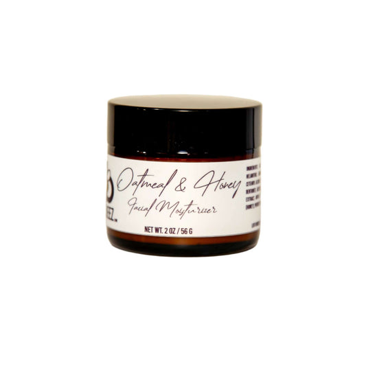 A small, round brown jar with a black lid contains "Oatmeal & Honey Facial Moisturizer" from Diaz Beez, blended with Sunflower Seed Oil. The label on the jar reads "2 oz / 56 g" and displays the product name in cursive script. The jar is photographed against a plain, light background.