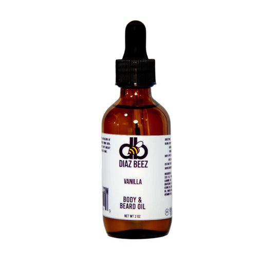 A 2 oz brown glass bottle with a dropper cap is labeled "Beard Taming Oil - Vanilla" by Diaz Beez. The label showcases a bee logo and black and purple text on a white background, emphasizing the infusion of natural fixed oils in this luxurious vanilla beard oil.