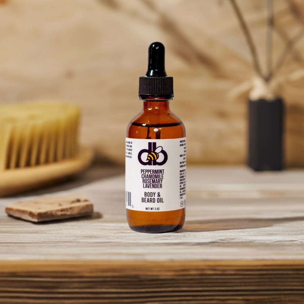 A bottle of Diaz Beez Beard Taming Oil, crafted with natural ingredients and essential oils such as Peppermint, Chamomile, Rosemary, and Lavender, complete with a dropper cap, rests on a wooden surface. In the blurred background, a wooden brush suggests an exquisite grooming setting.
